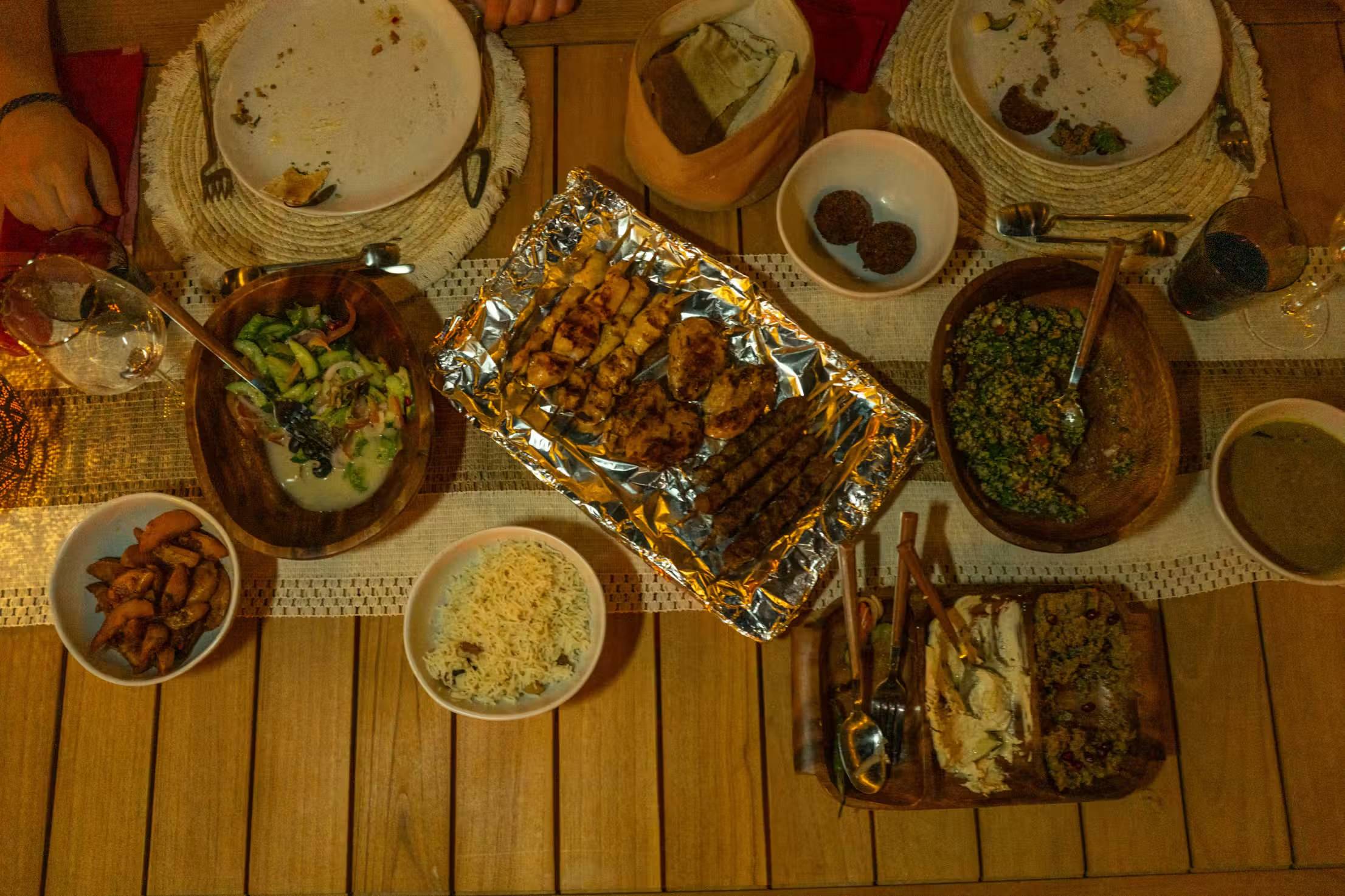 Grilled kebabs, rice, salads and dips served on a wooden table
